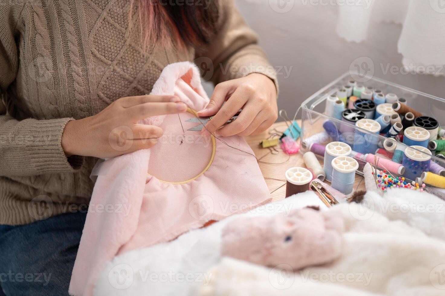 une fermer image de une femme en utilisant les ciseaux à Couper une fil sur un broderie Cadre. photo