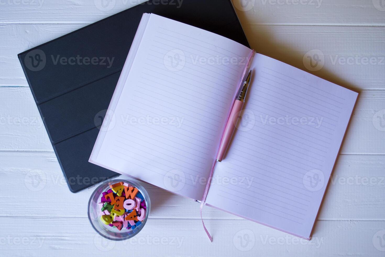 une bloc-notes avec stylo, rose cactus, froissé feuille de papier et multicolore des lettres sur une blanc en bois bureau. photo
