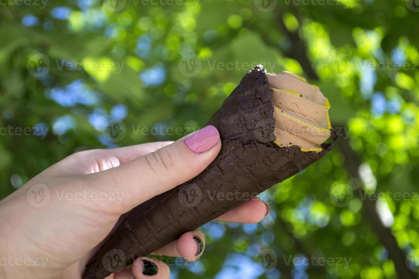 un la glace crème cône dans femelle bras contre une vert arbre Contexte photo