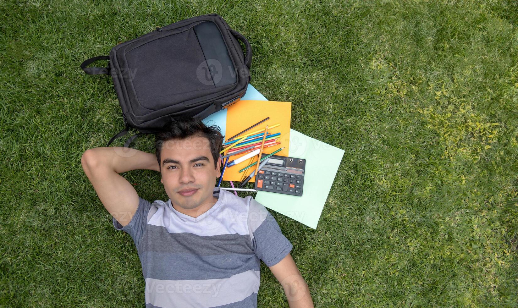 une Masculin étudiant mensonge sur le herbe avec une sac à dos et une calculatrice photo