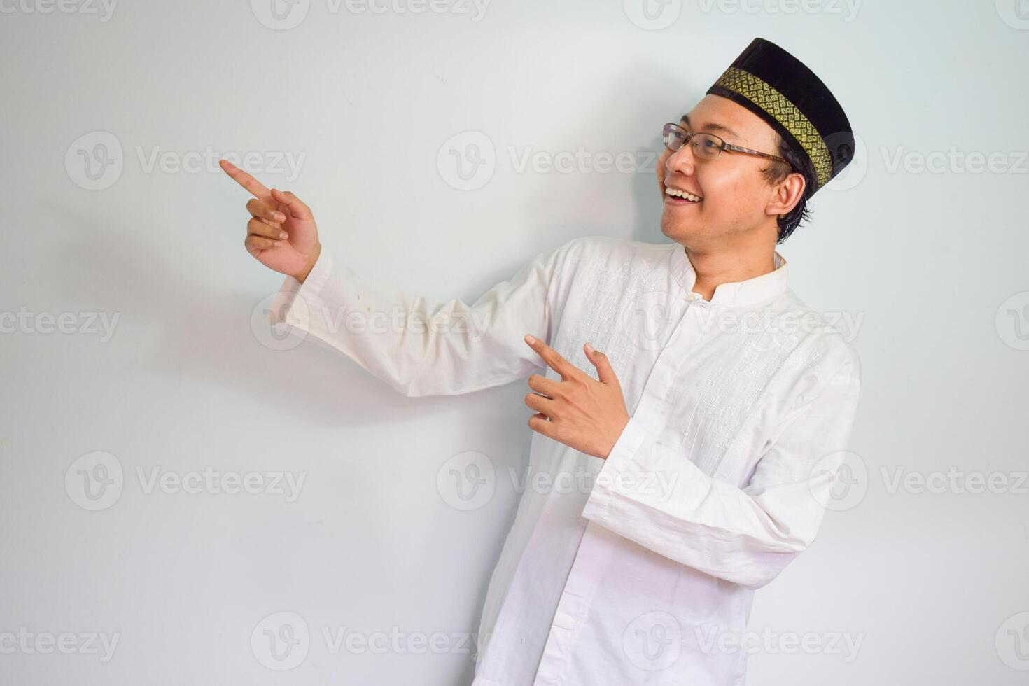 asiatique musulman homme portant des lunettes et blanc tissu souriant et montrer du doigt pose pour ramadhan et eid Al fitr. isolé blanc Contexte photo