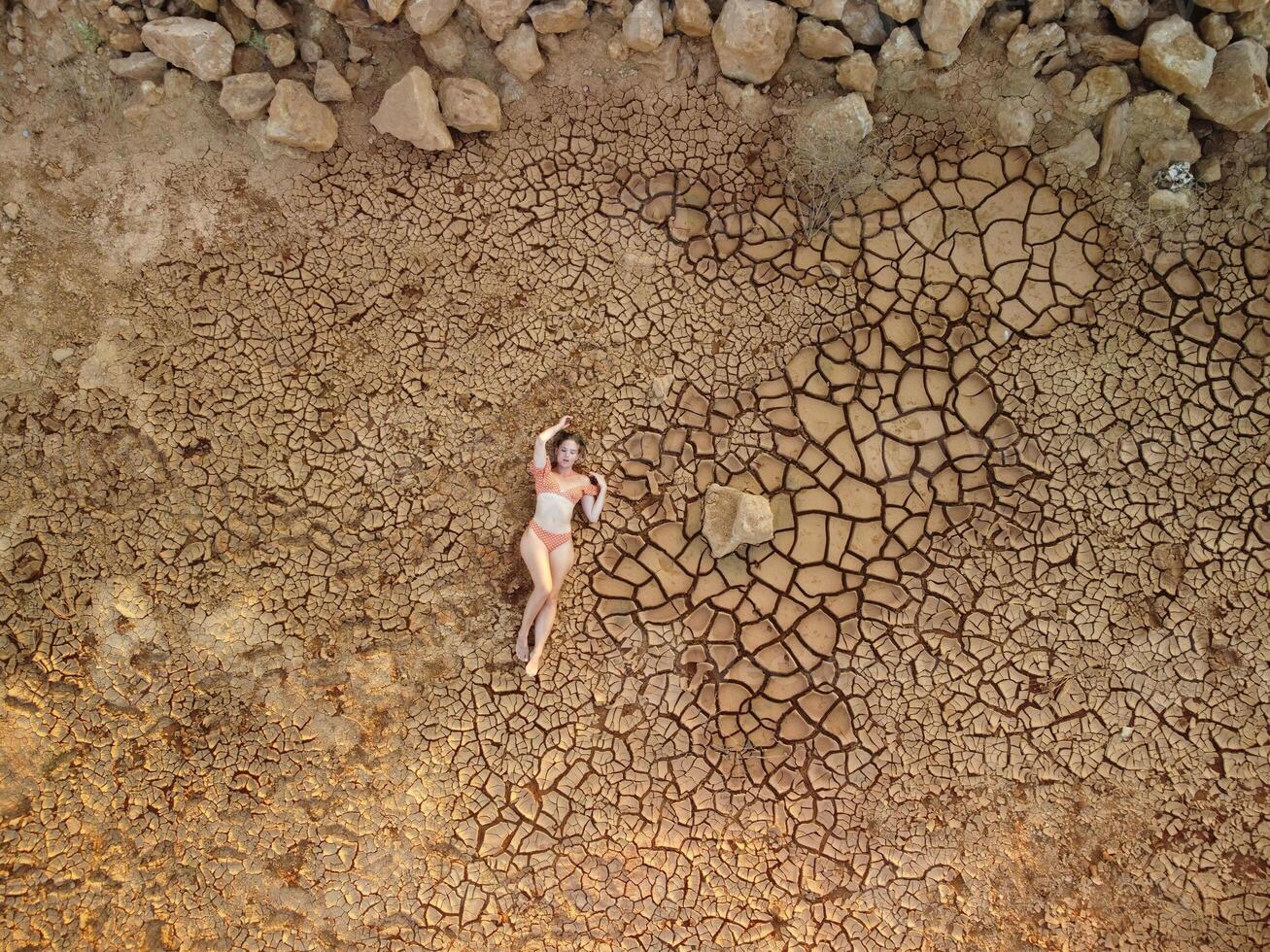 aérien portrait de magnifique Jeune Dame dans bikini mensonge sur sec fissuré rouge sol. aride, fissuré rouge sol sécheresse et aride climat conditions. climat et temps changement. photo