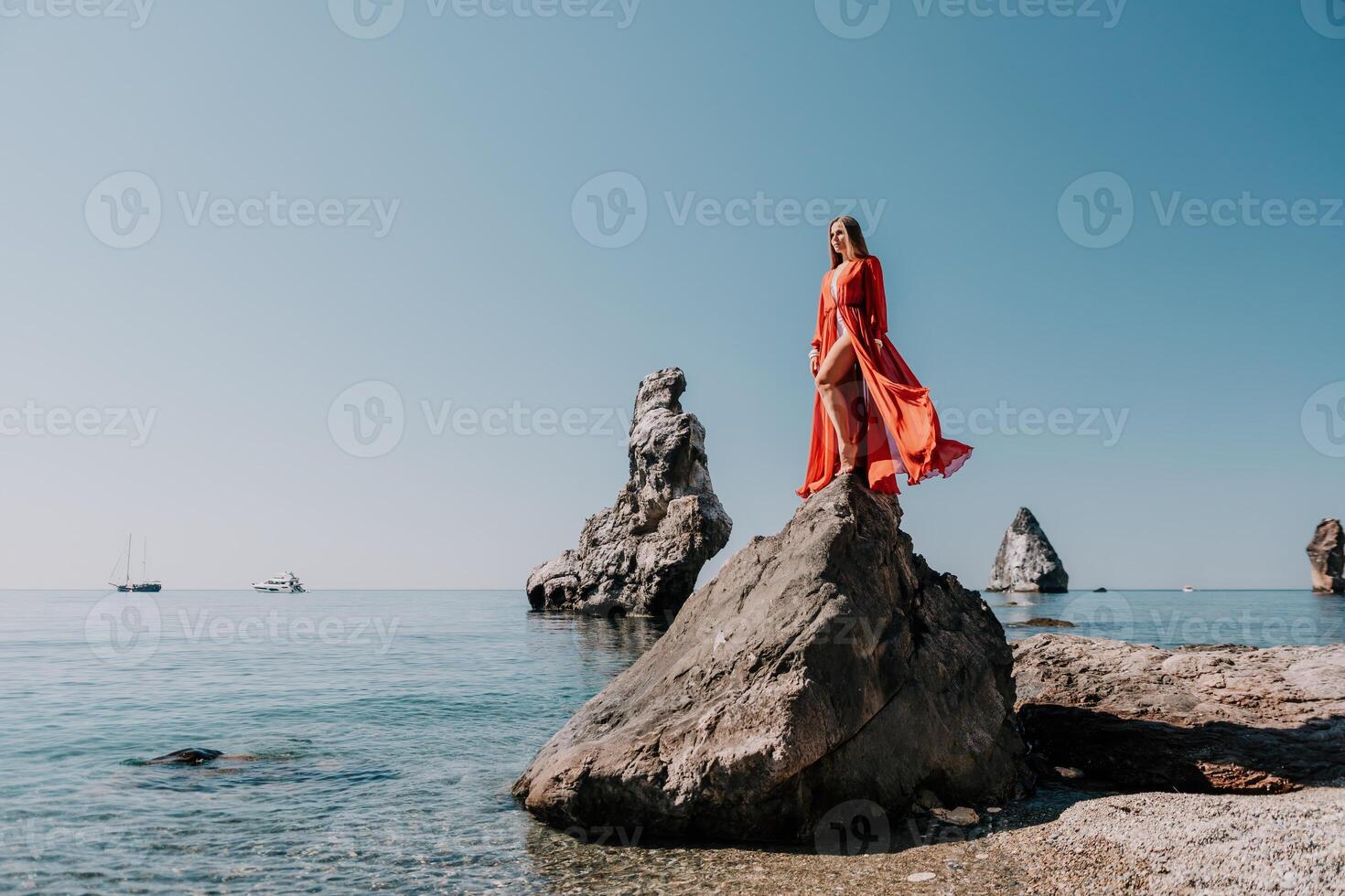 femme Voyage mer. Jeune content femme dans une longue rouge robe posant sur une plage près le mer sur Contexte de volcanique rochers, comme dans Islande, partage Voyage aventure périple photo