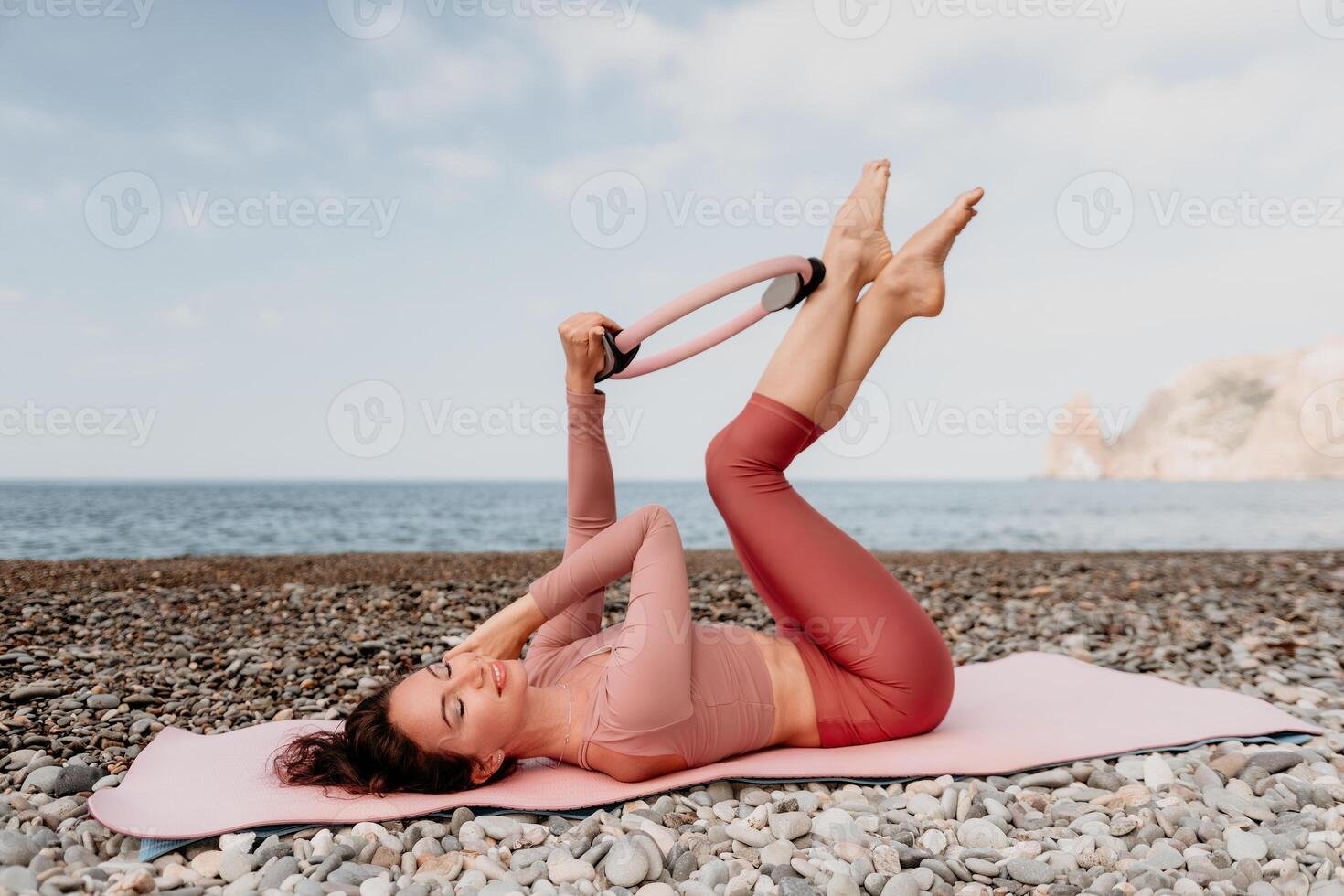 femme mer pilates. sportif content milieu vieilli femme pratiquant aptitude sur plage près mer, souriant actif femelle formation avec bague sur yoga tapis dehors, profiter en bonne santé mode de vie, harmonie et méditation photo