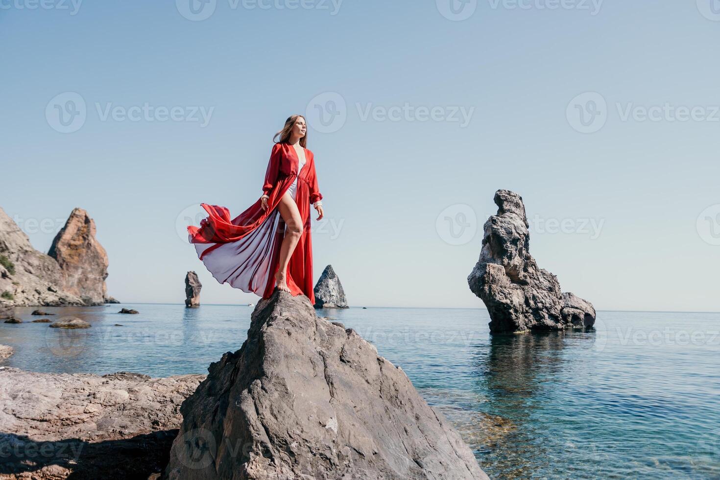 femme Voyage mer. Jeune content femme dans une longue rouge robe posant sur une plage près le mer sur Contexte de volcanique rochers, comme dans Islande, partage Voyage aventure périple photo