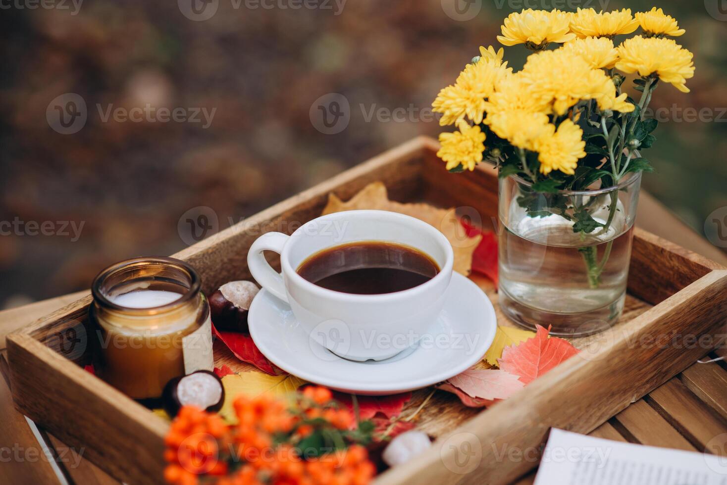 une tasse de thé ou café sur une en bois plateau contre le l'automne Contexte avec déchue feuilles, bougie et fleurs, l'automne ambiance photo