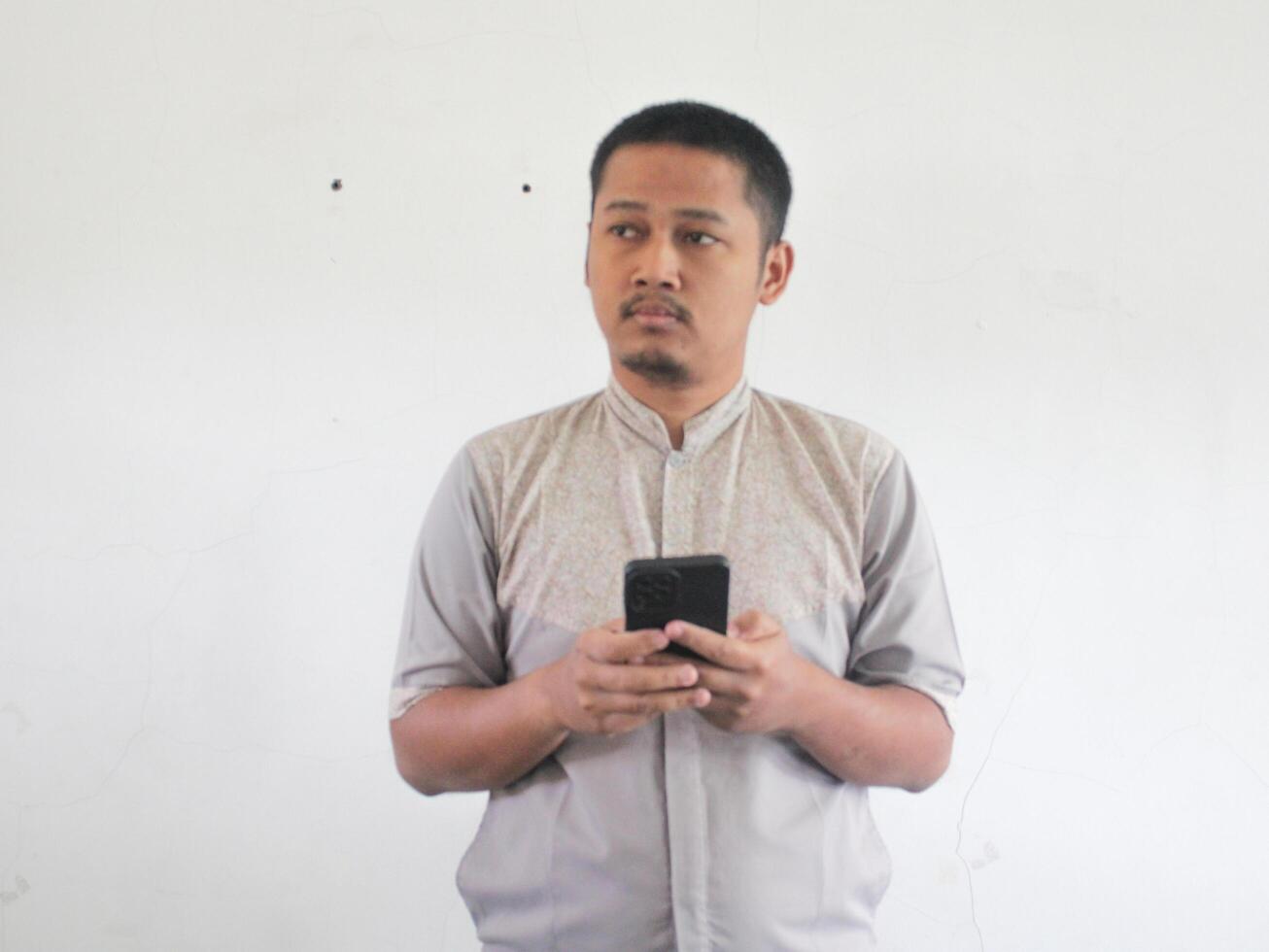 asiatique homme en portant le sien mobile téléphone avec sérieux expression photo