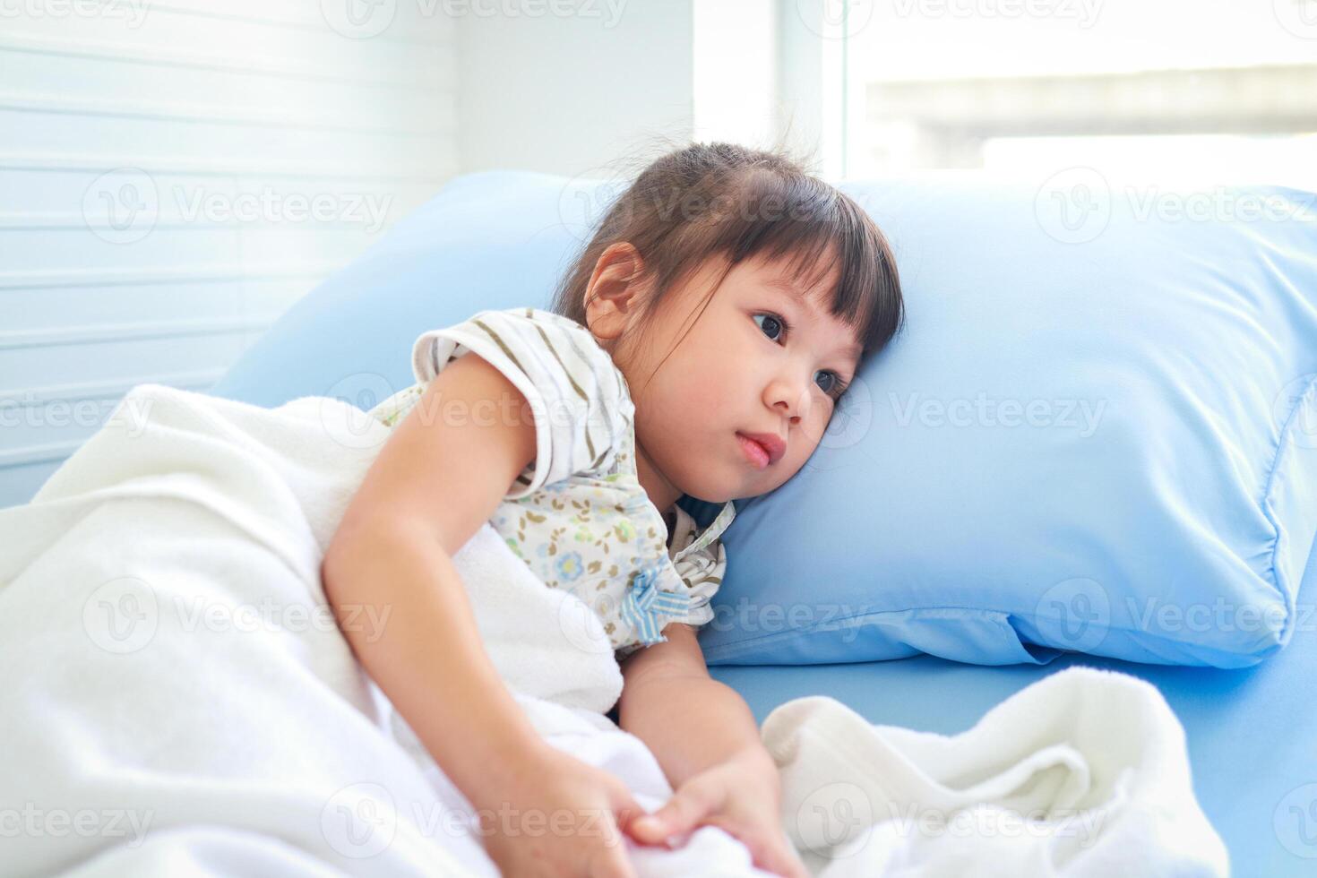 une peu asiatique fille est malade avec une fièvre. elle a été mensonge sur le lit dans le hôpital examen chambre. concept de enfants maladie, viral infection, médical prestations de service photo