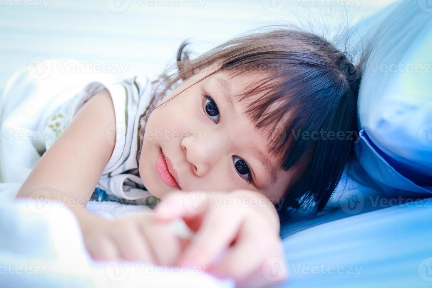 une peu asiatique fille est malade avec une fièvre. elle a été mensonge sur le lit dans le hôpital examen chambre. concept de enfants maladie, viral infection, médical prestations de service photo