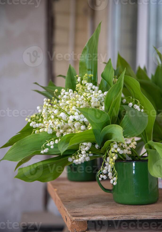 encore la vie dans rustique style avec bouquets de fleurs de lys de le vallée dans vert émaillé ancien tasses, floral Contexte photo