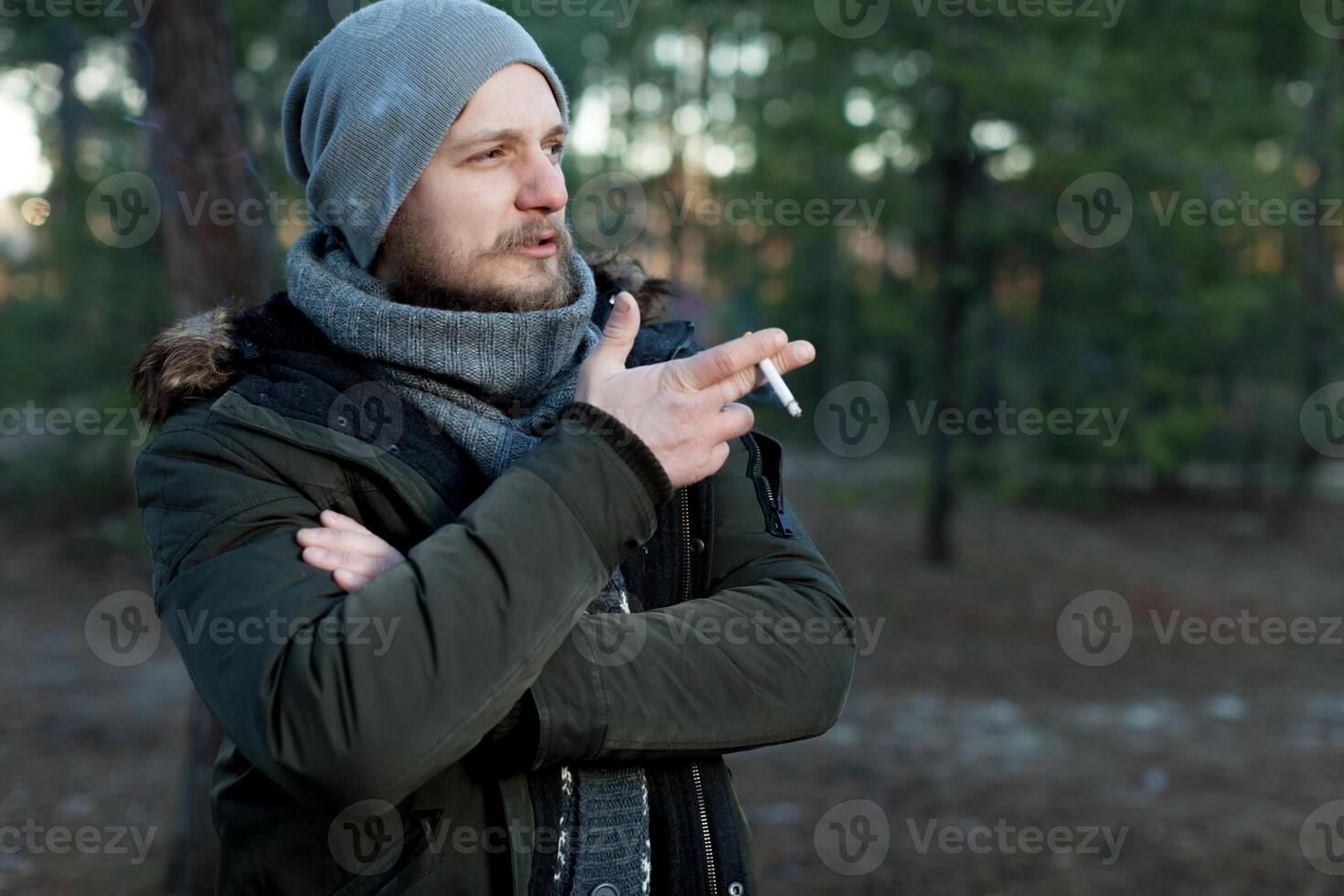 Beau sexy barbu Jeune homme branché avec longue barbe et moustache a élégant cheveux sur sérieux poilu visage fumeur cigarette Extérieur sur vert Naturel Contexte photo