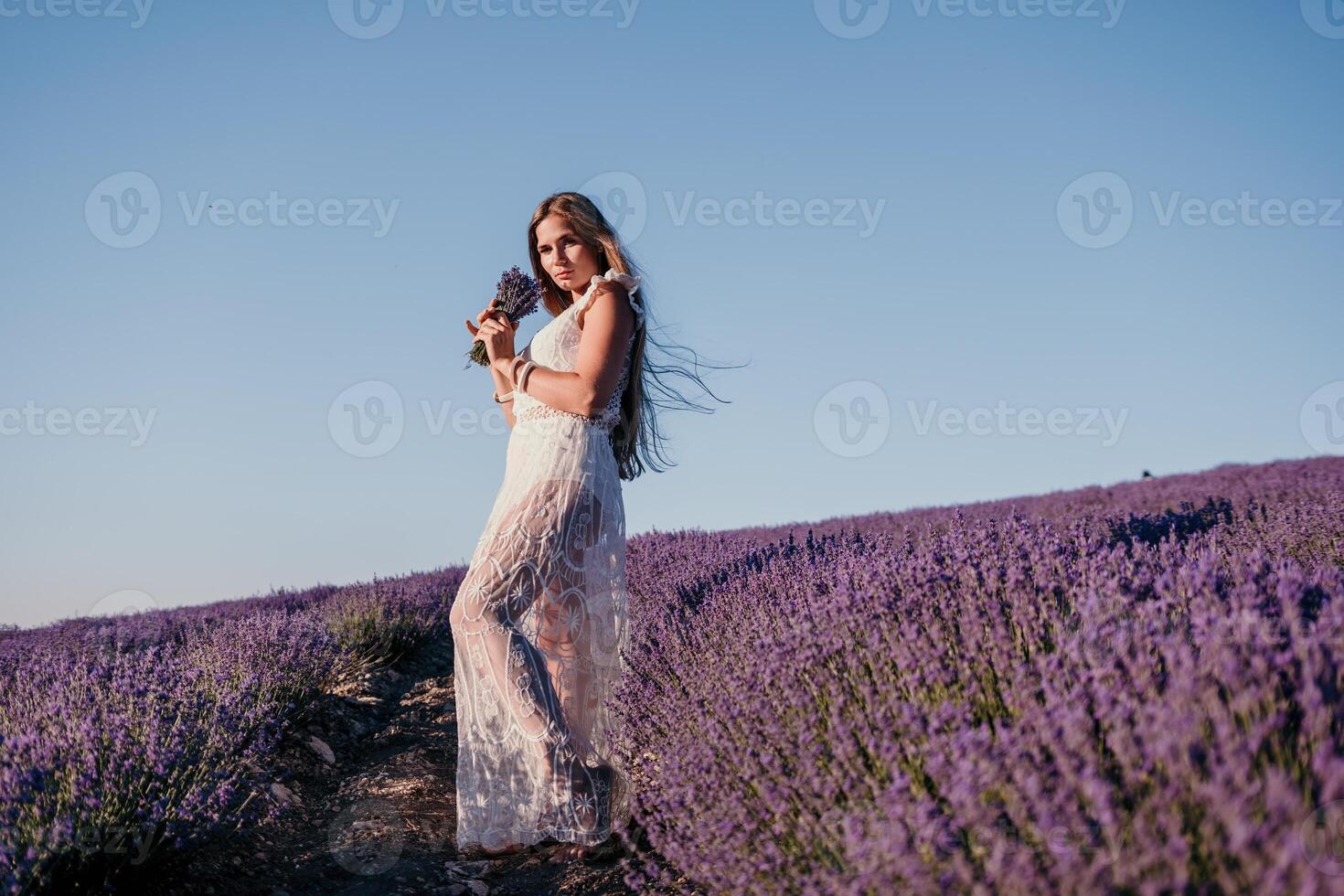 femme lavande champ. content insouciant femme dans une blanc robe en marchant dans une lavande champ et odeur une lavande bouquet sur le coucher du soleil. idéal pour chaud et inspirant concepts dans esprit d'aventure et Voyage. photo