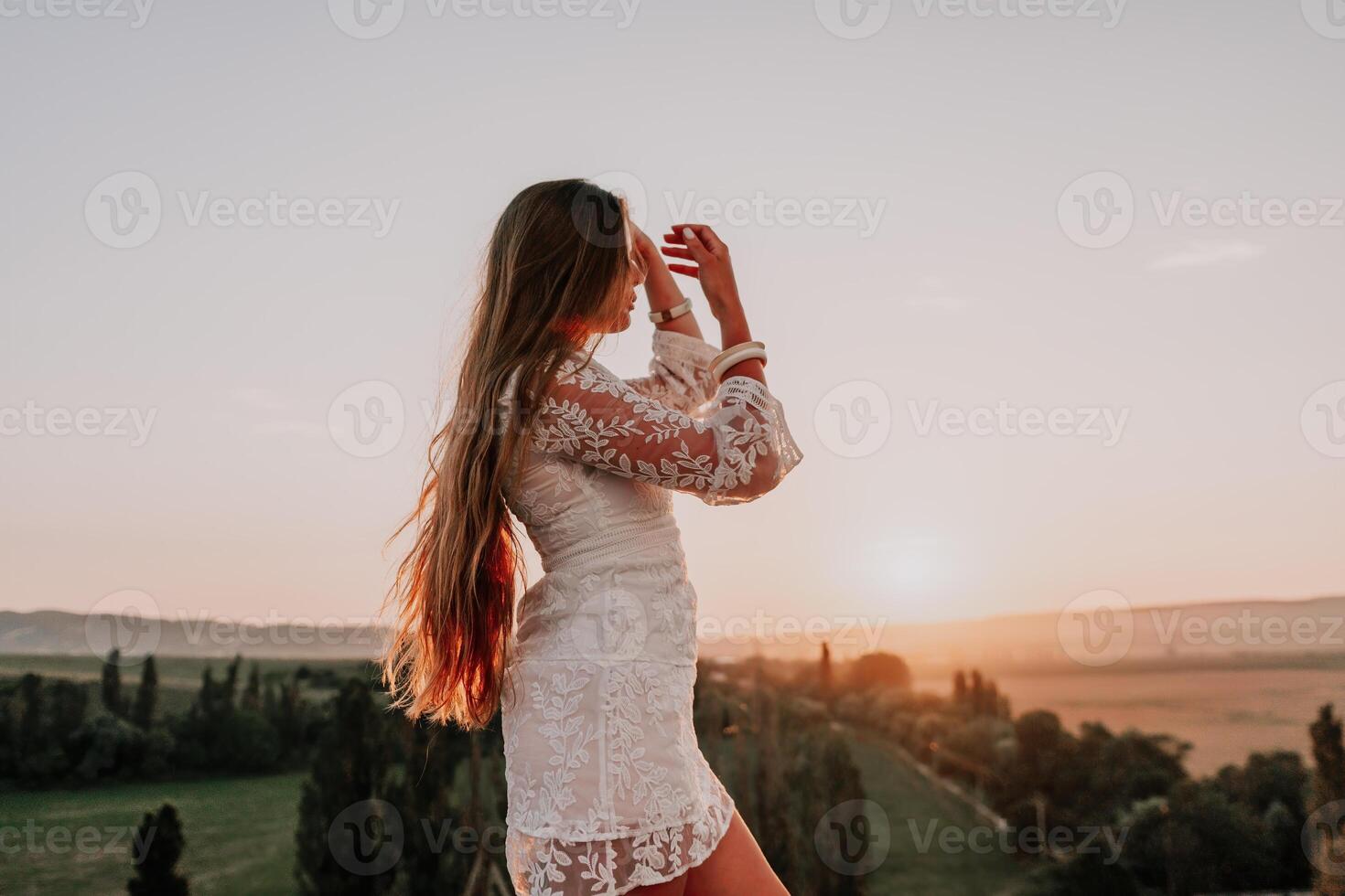 content femme dans blanc boho robe sur le coucher du soleil dans montagnes. romantique femme avec longue cheveux permanent avec sa retour sur le le coucher du soleil dans la nature dans été avec ouvert mains. silhouette. la nature. le coucher du soleil. photo