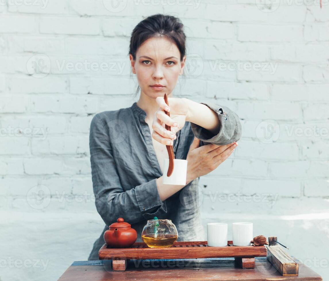 Oriental Maître de thé la cérémonie avec blanc brique mur sur le Contexte. traditionnel thé fête sur le la nature avec femme habillé dans le gris chemise photo