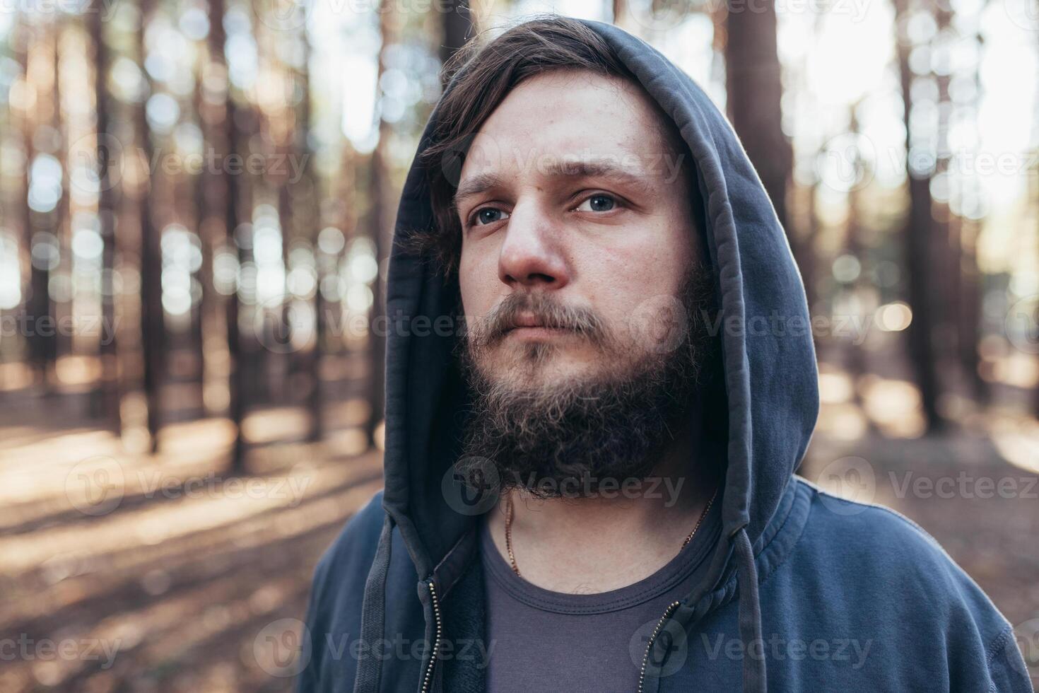 une Jeune homme avec une barbe des promenades dans une pin forêt. portrait de une brutal barbu homme dans une capuche photo