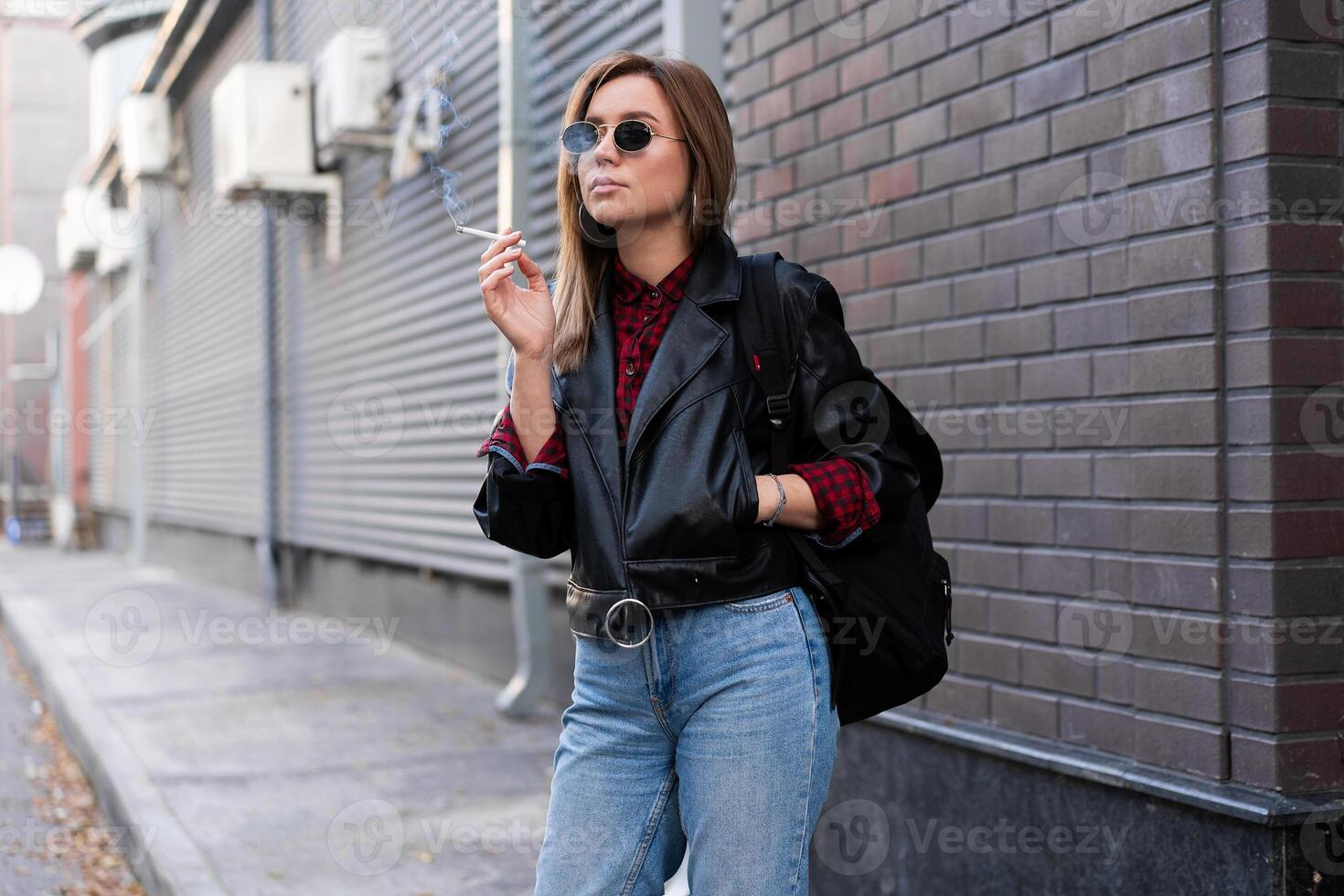 magnifique Jeune avec style habillé caucasien fille fume cigarette sur le rue. photo