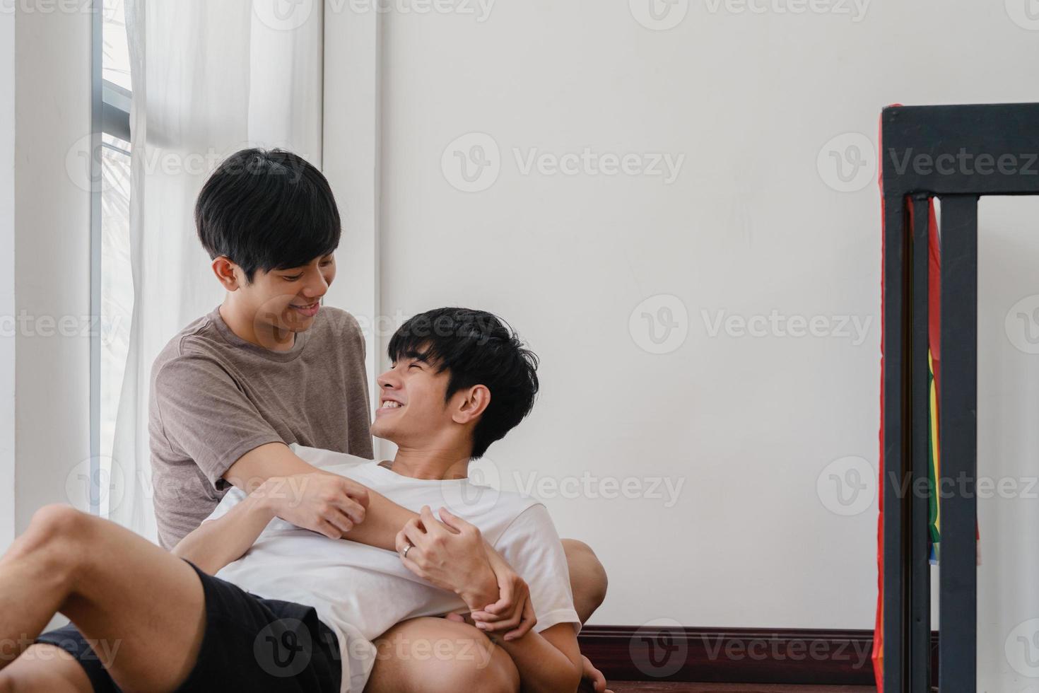 couple gay asiatique allongé et s'embrassant sur le sol à la maison. jeunes hommes lgbtq asiatiques s'embrassant heureux se détendre se reposer ensemble passer du temps romantique dans le salon avec drapeau arc-en-ciel dans une maison moderne le matin. photo