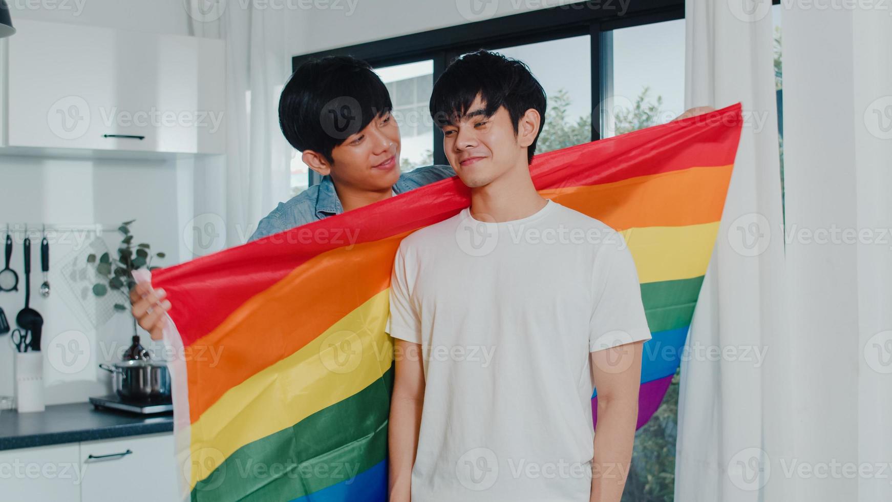 couple gay asiatique debout et étreignant la chambre à la maison. jeunes beaux hommes lgbtq s'embrassant heureux se détendre ensemble passer du temps romantique dans une cuisine moderne avec drapeau arc-en-ciel à la maison le matin concept. photo