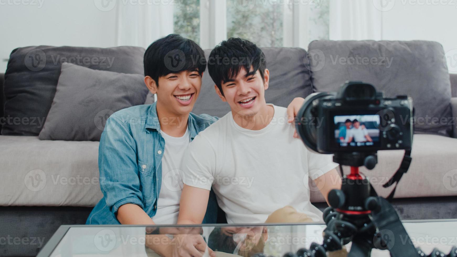 jeune couple gay asiatique couple d'influenceurs vlog à la maison. les adolescents coréens lgbtq heureux se détendent en s'amusant à l'aide de l'enregistrement de la caméra vlog vidéo upload dans les médias sociaux tout en étant allongé sur le canapé dans le salon au concept de maison. photo