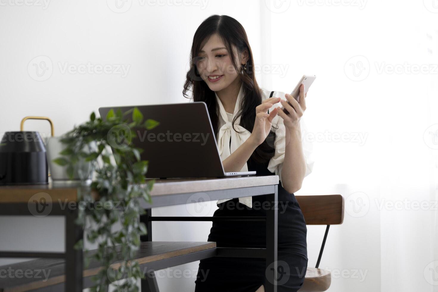 une Japonais femme vérification téléphone intelligent par éloigné travail dans le Accueil Bureau photo