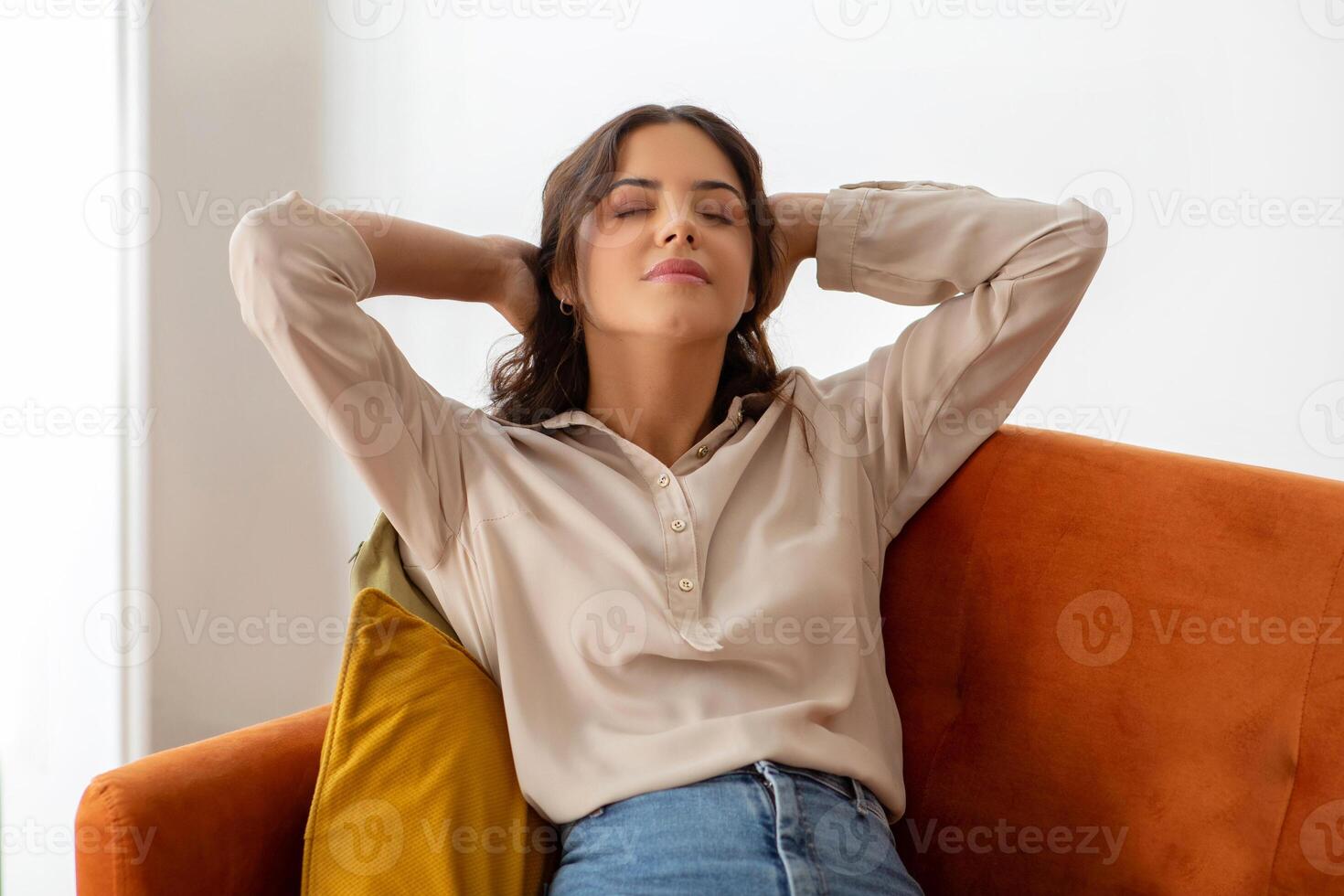 serein Jeune femme avec mains derrière tête repos sur canapé à Accueil photo