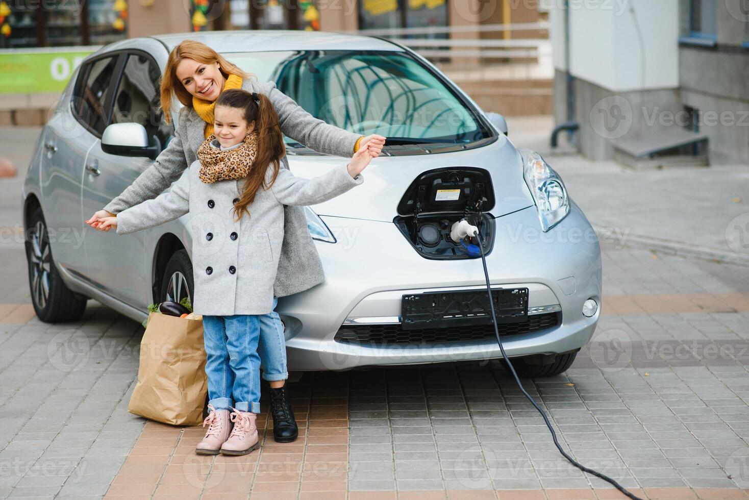 mère avec fille mise en charge électro voiture à le électrique gaz station et parler sur mobile téléphone photo