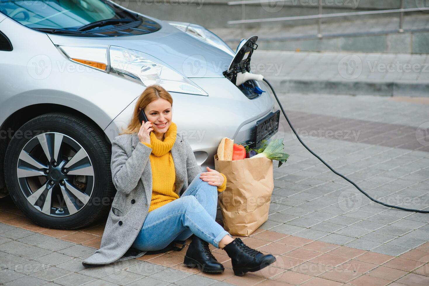 en utilisant un smartphone en attendant. femme sur la station de charge des voitures électriques pendant la journée. véhicule neuf photo