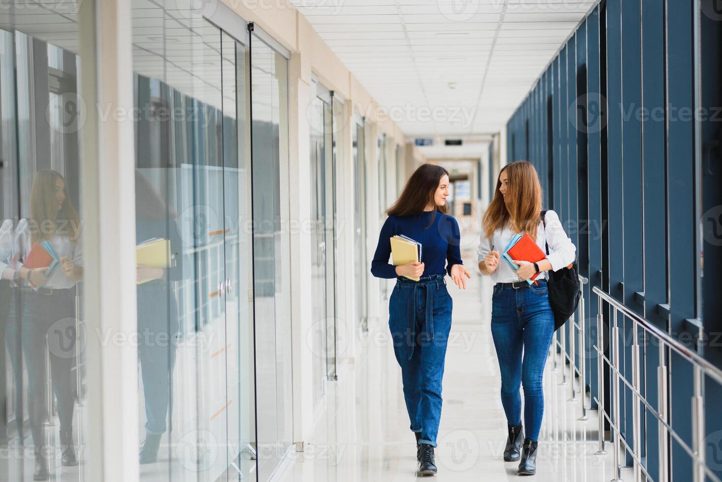 deux Jeune femmes avec livre bavardage tandis que permanent dans Université couloir. Université élèves dans couloir après le conférence. photo