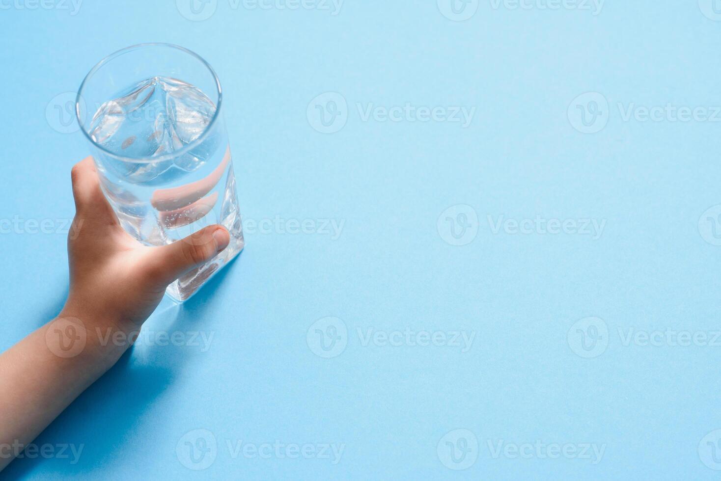 enfants main en portant une verre de pur l'eau sur une bleu arrière-plan, copie espace photo