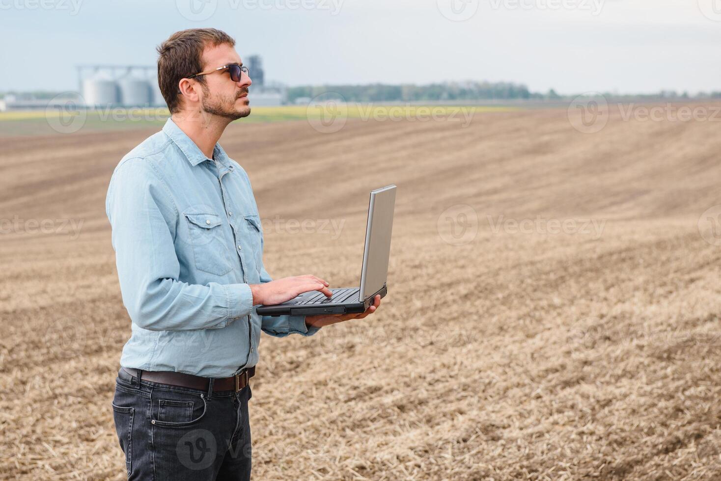 content agriculteur avec portable permanent dans blé champ dans de face de grain silo photo