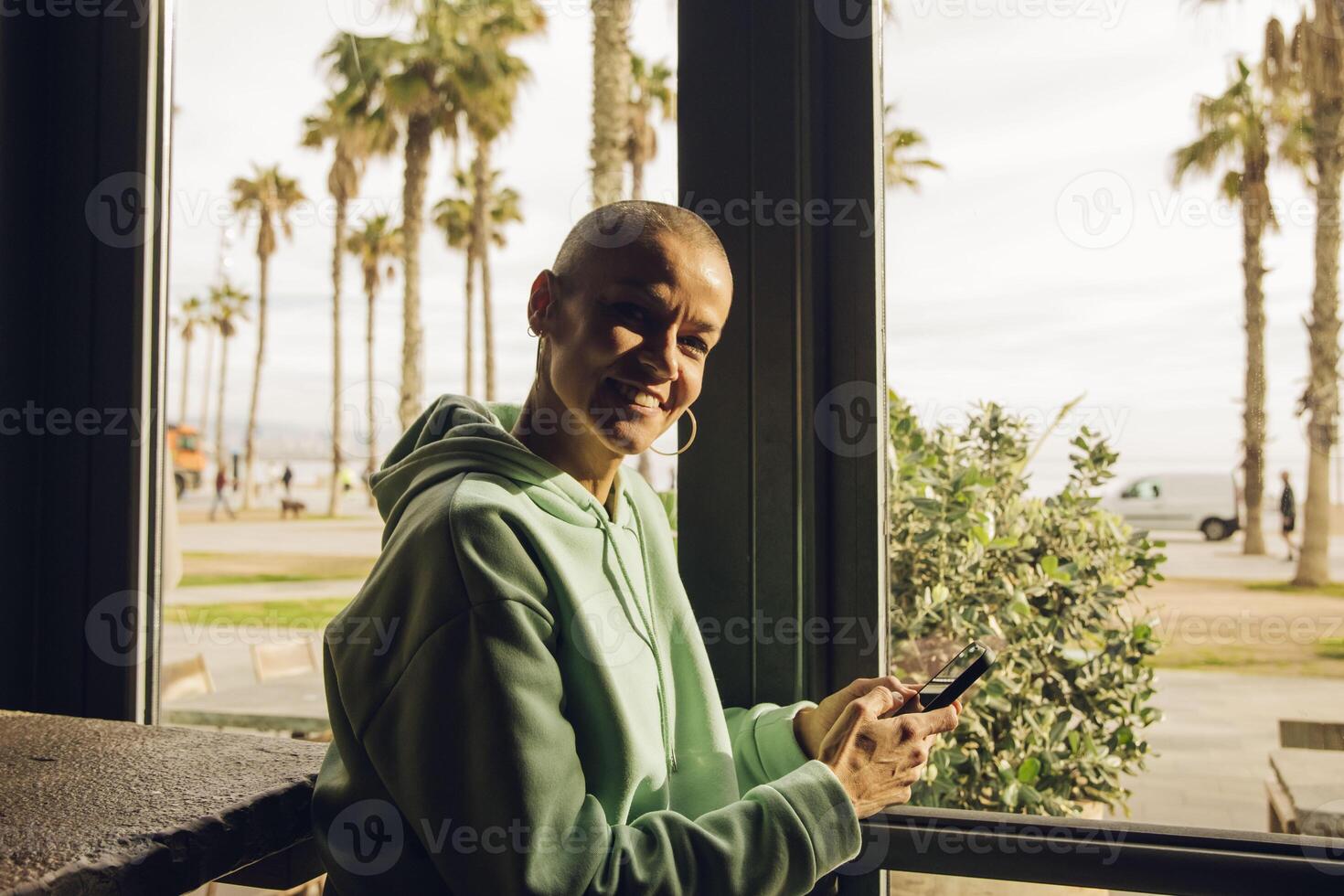 femme avec une chauve cheveux style souriant en utilisant une dispositif intérieur photo