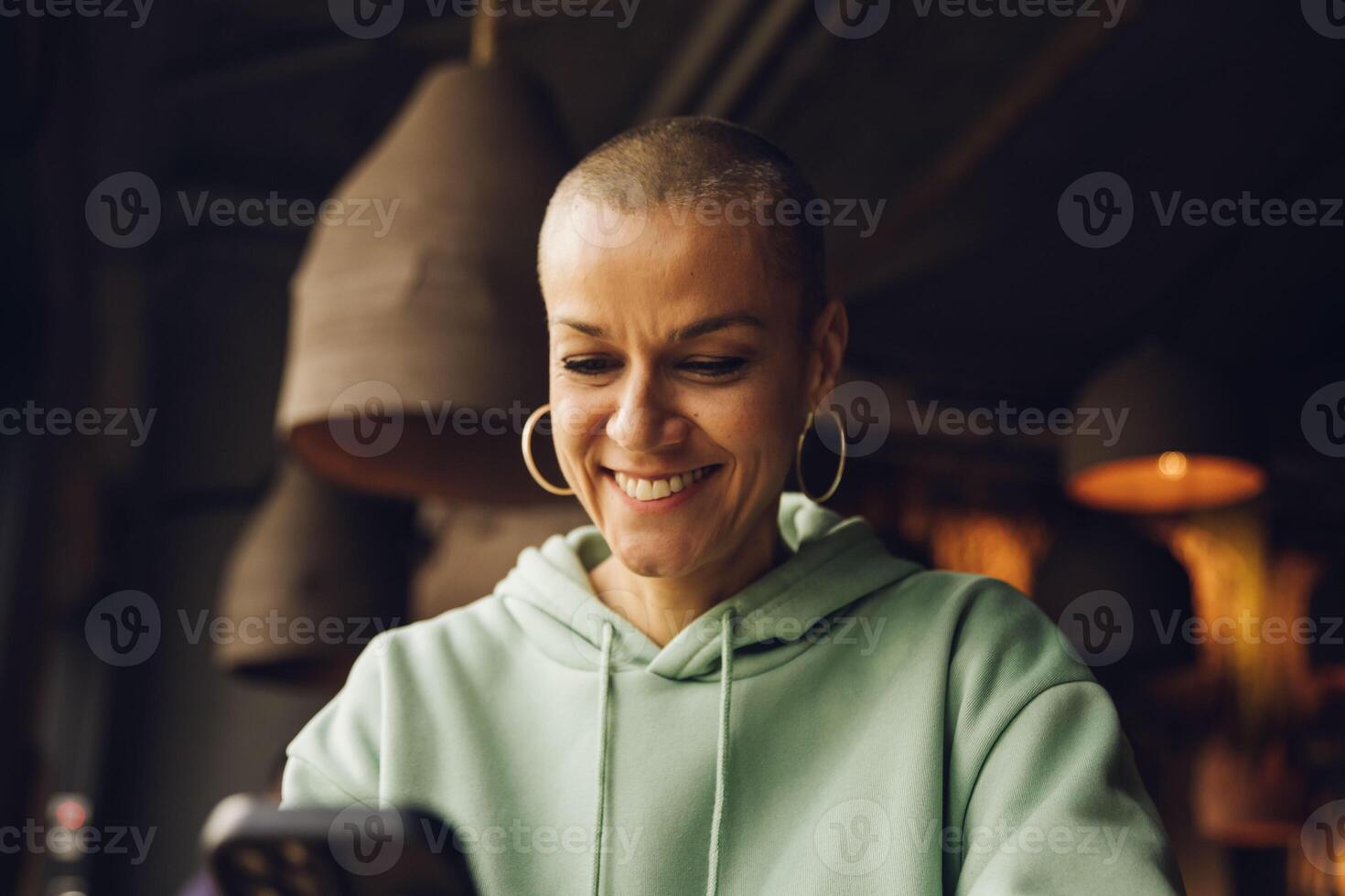 femme avec une chauve cheveux style souriant en utilisant une dispositif intérieur photo