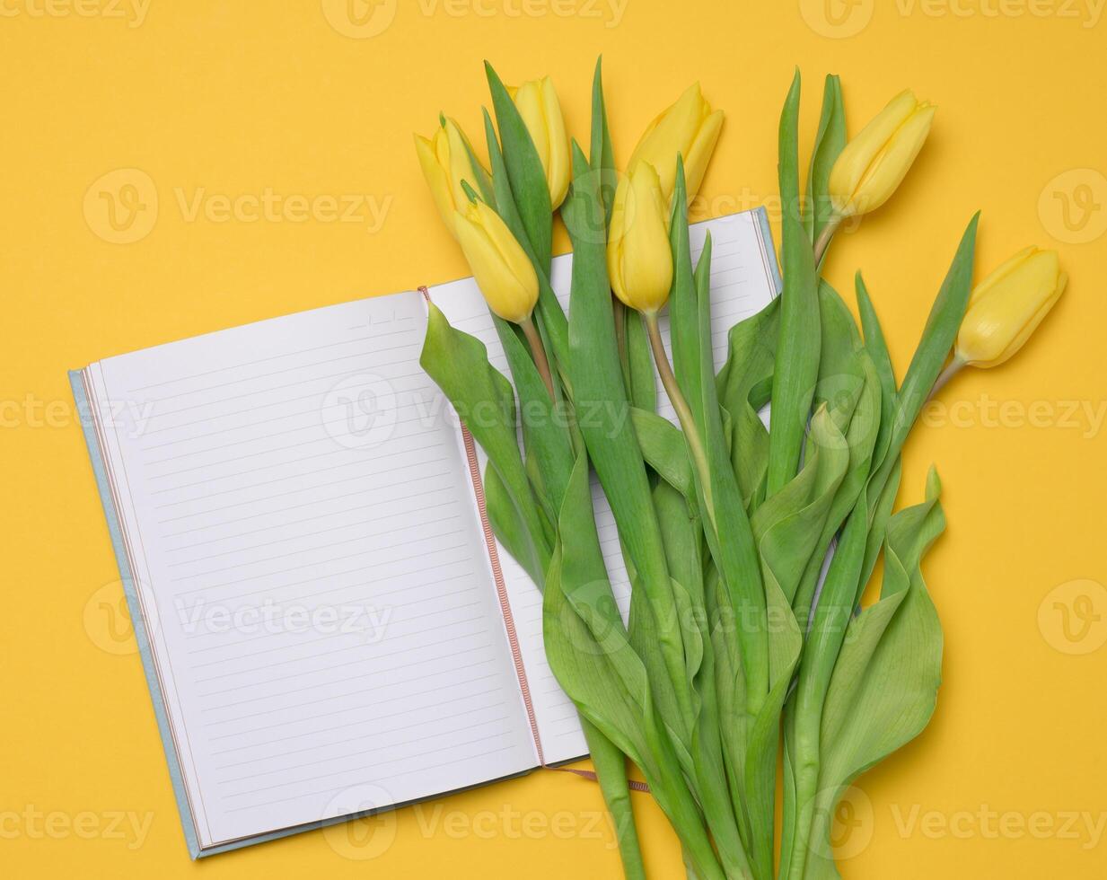 ouvert carnet avec blanc Vide feuilles et une bouquet de Jaune tulipes sur une Jaune Contexte photo