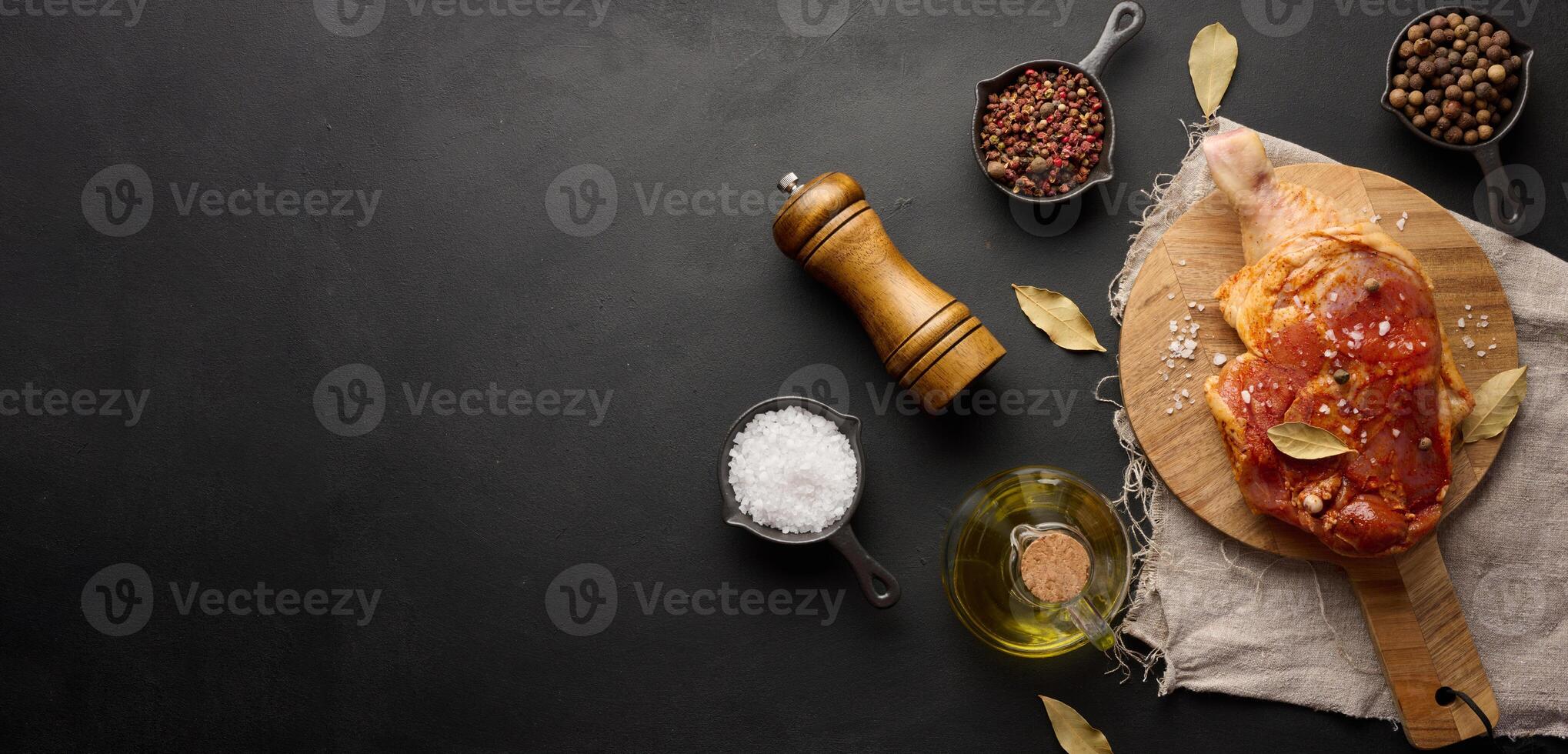 brut poulet pilons chevronné sur une en bois conseil, accompagné par sel et poivres, vu de le Haut. noir table photo