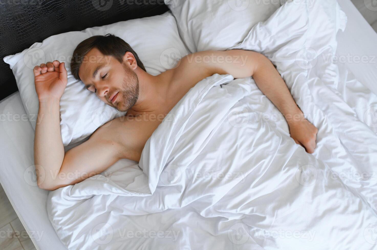 Beau homme en train de dormir en dessous de doux couverture dans lit à Accueil photo