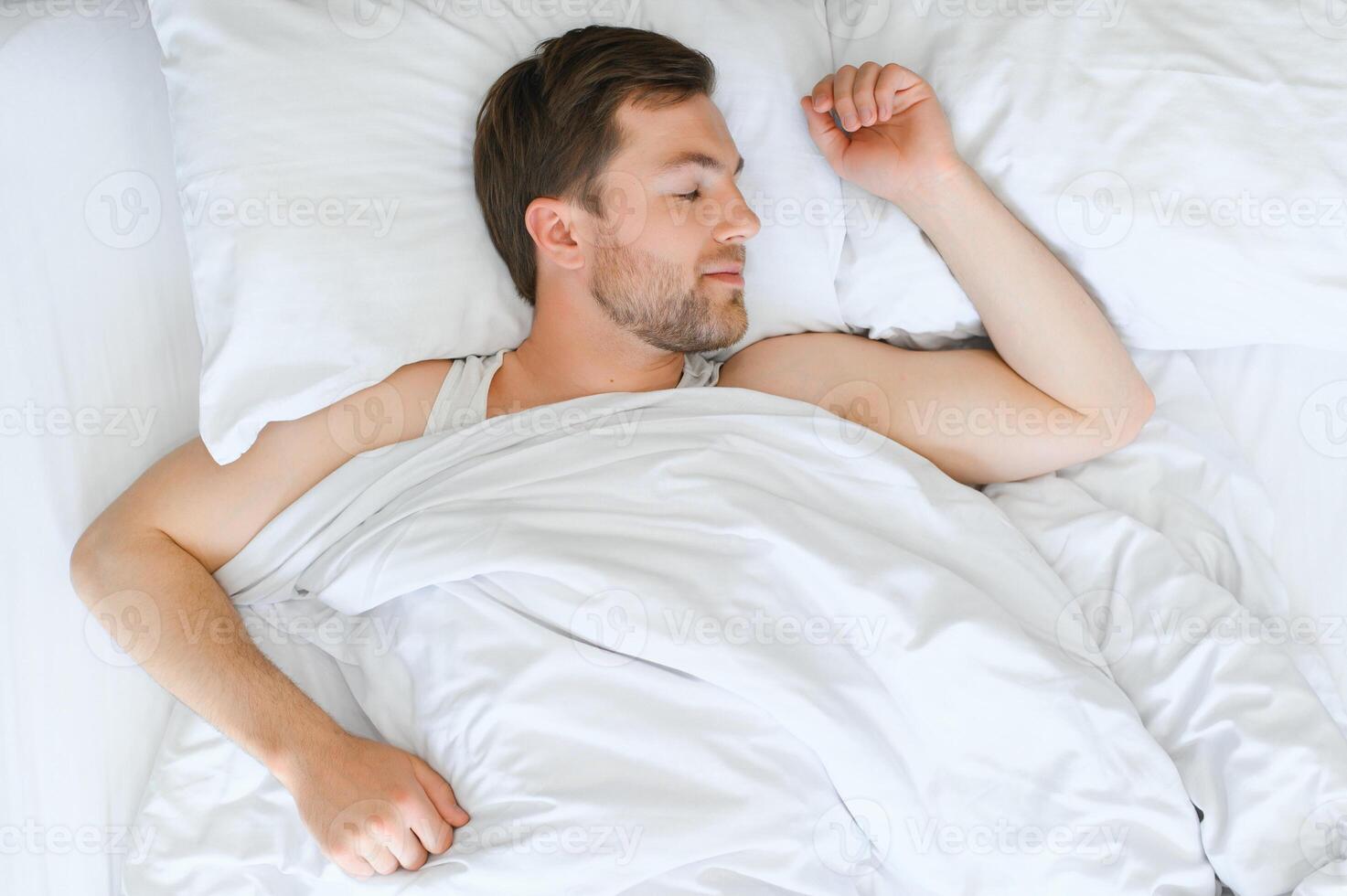 Beau homme en train de dormir en dessous de doux couverture dans lit à Accueil photo