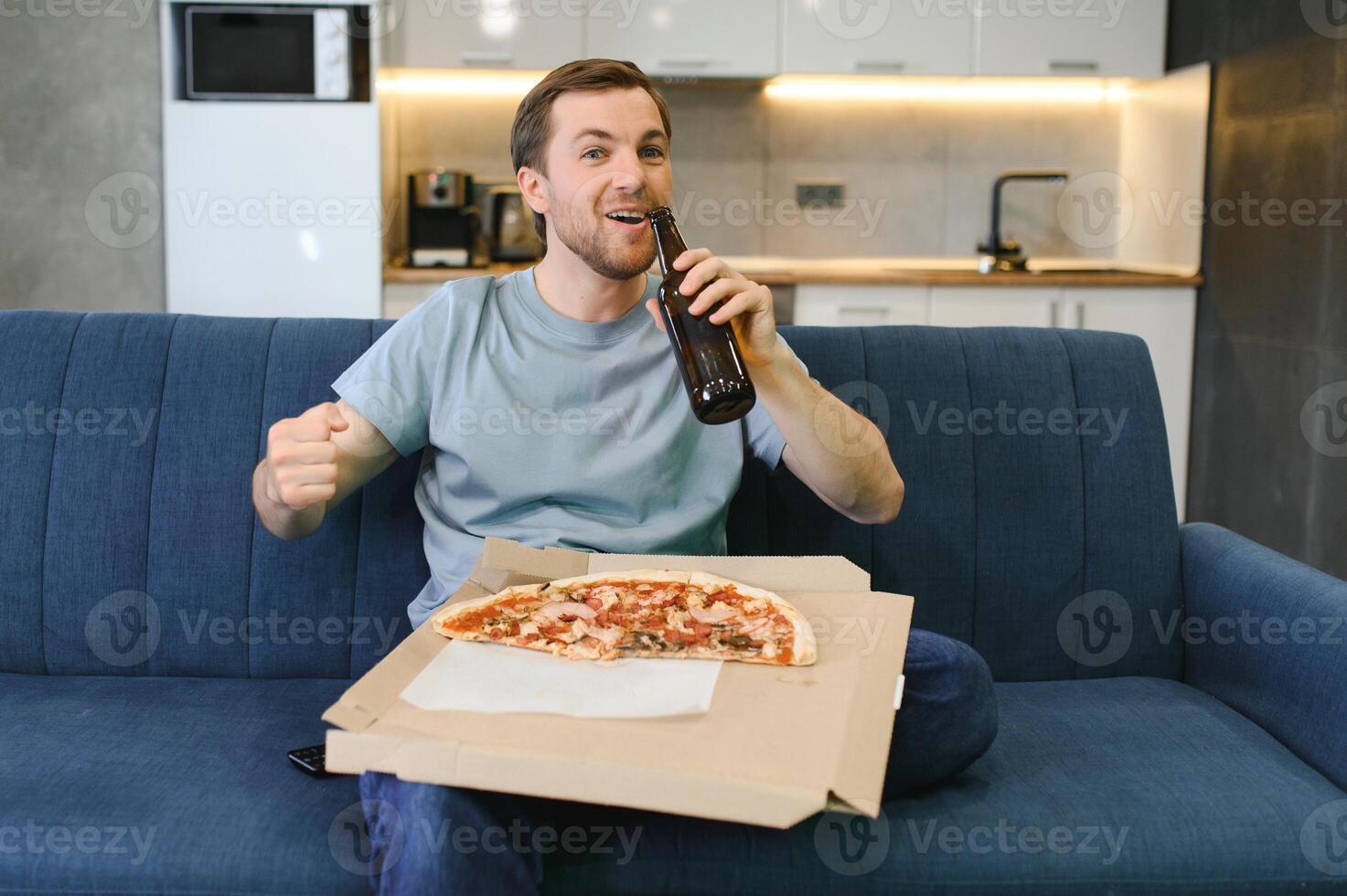 content Jeune homme en buvant Bière et en mangeant Pizza lorsque en train de regarder Jeu sur la télé à Accueil photo