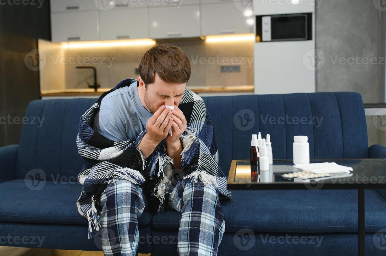 malade homme sur canapé à Accueil dans vivant chambre. homme sentiment malade avec du froid et fièvre à maison, mauvais avec grippe maladie séance sur le canapé. c'est le saison de éternue. photo