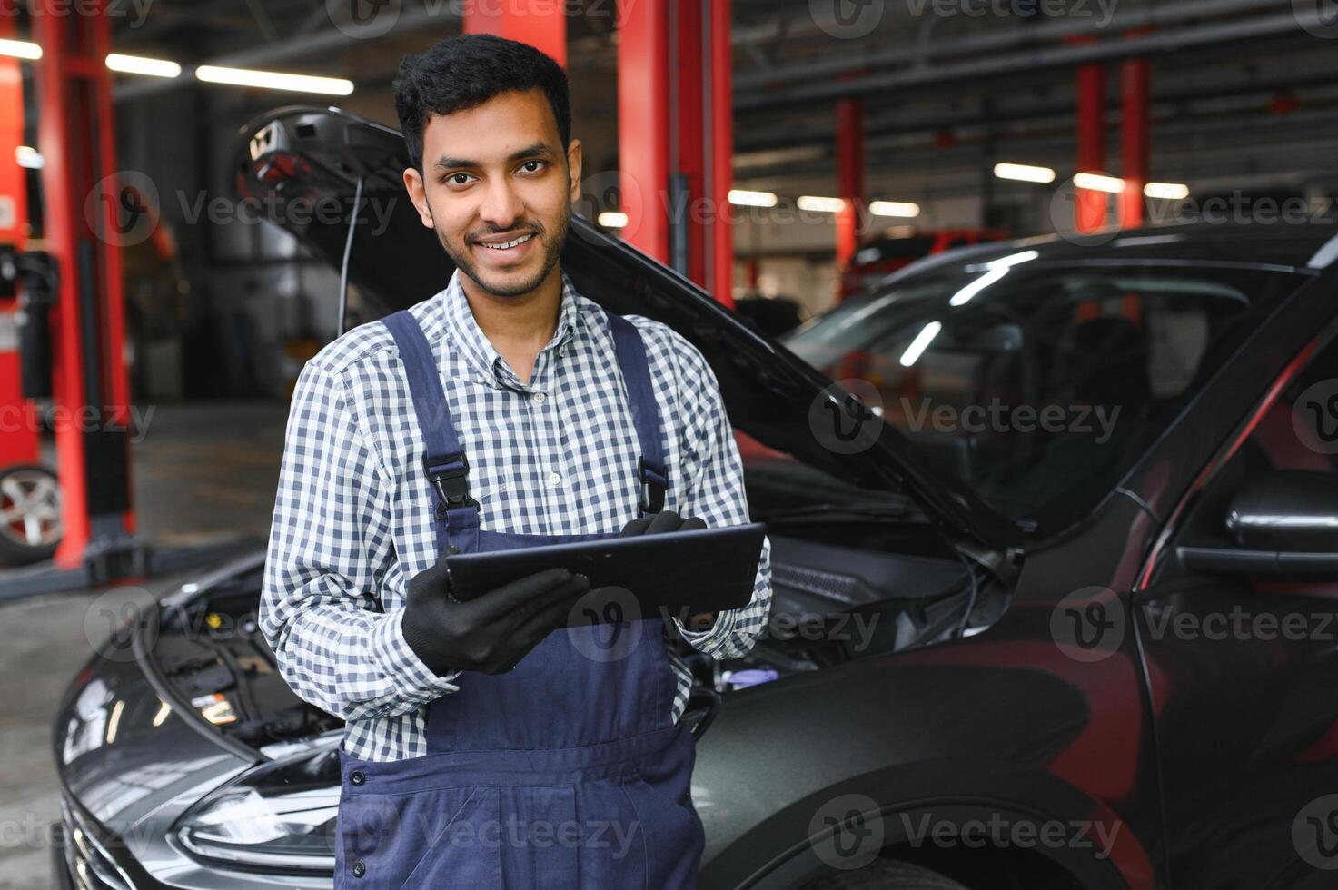 mécanicien homme mécanicien directeur ouvrier en utilisant une portable ordinateur vérification voiture dans atelier à auto voiture réparation un service centre. ingénieur Jeune homme à la recherche à inspection véhicule détails en dessous de voiture capot. photo