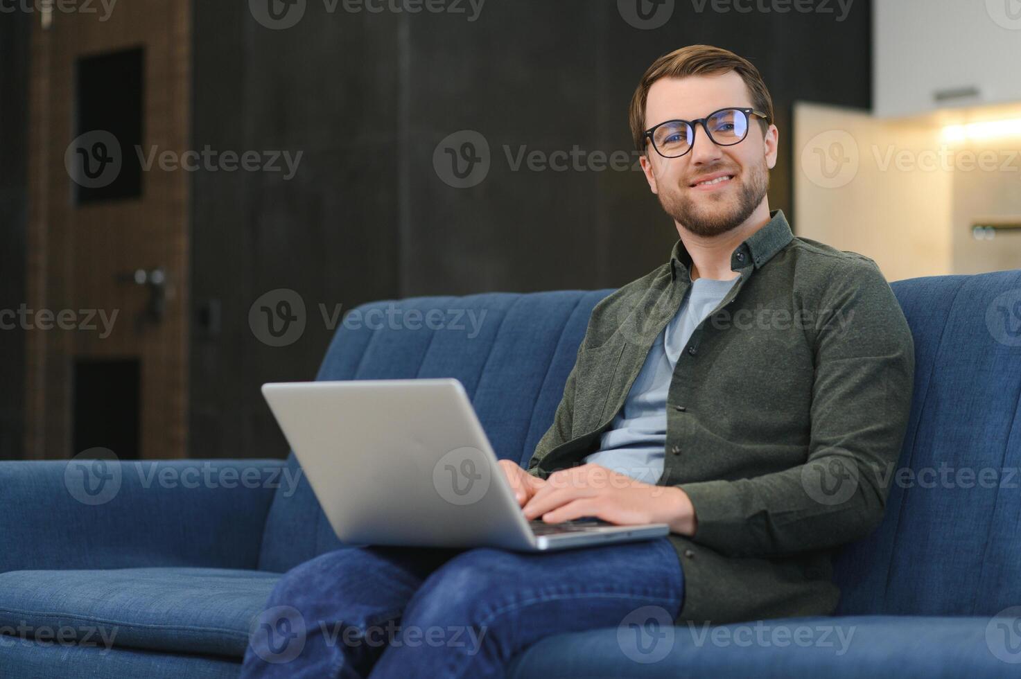 côté vue Beau Jeune homme d'affaire dans lunettes travail avec ordinateur. agréable content homme communicant dans social réseau, recherche information en ligne photo