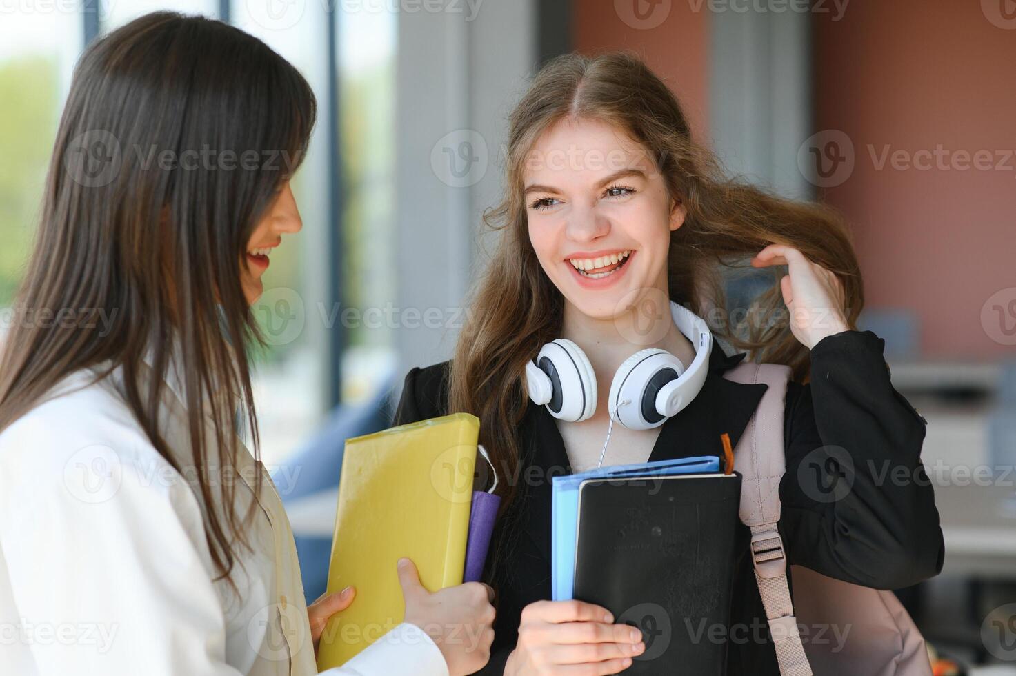 deux Jeune femmes avec livre bavardage tandis que permanent dans Université couloir. Université élèves dans couloir après le conférence photo