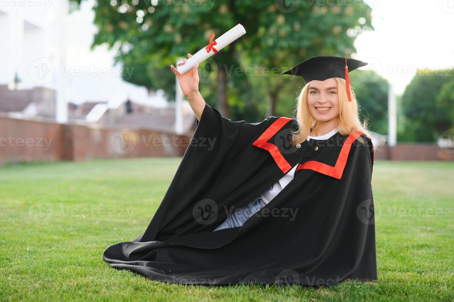 content mignonne caucasien grad fille est souriant. elle est dans une noir mortier conseil, avec rouge gland, dans robe, avec agréable marron frisé cheveux, diplôme dans main photo