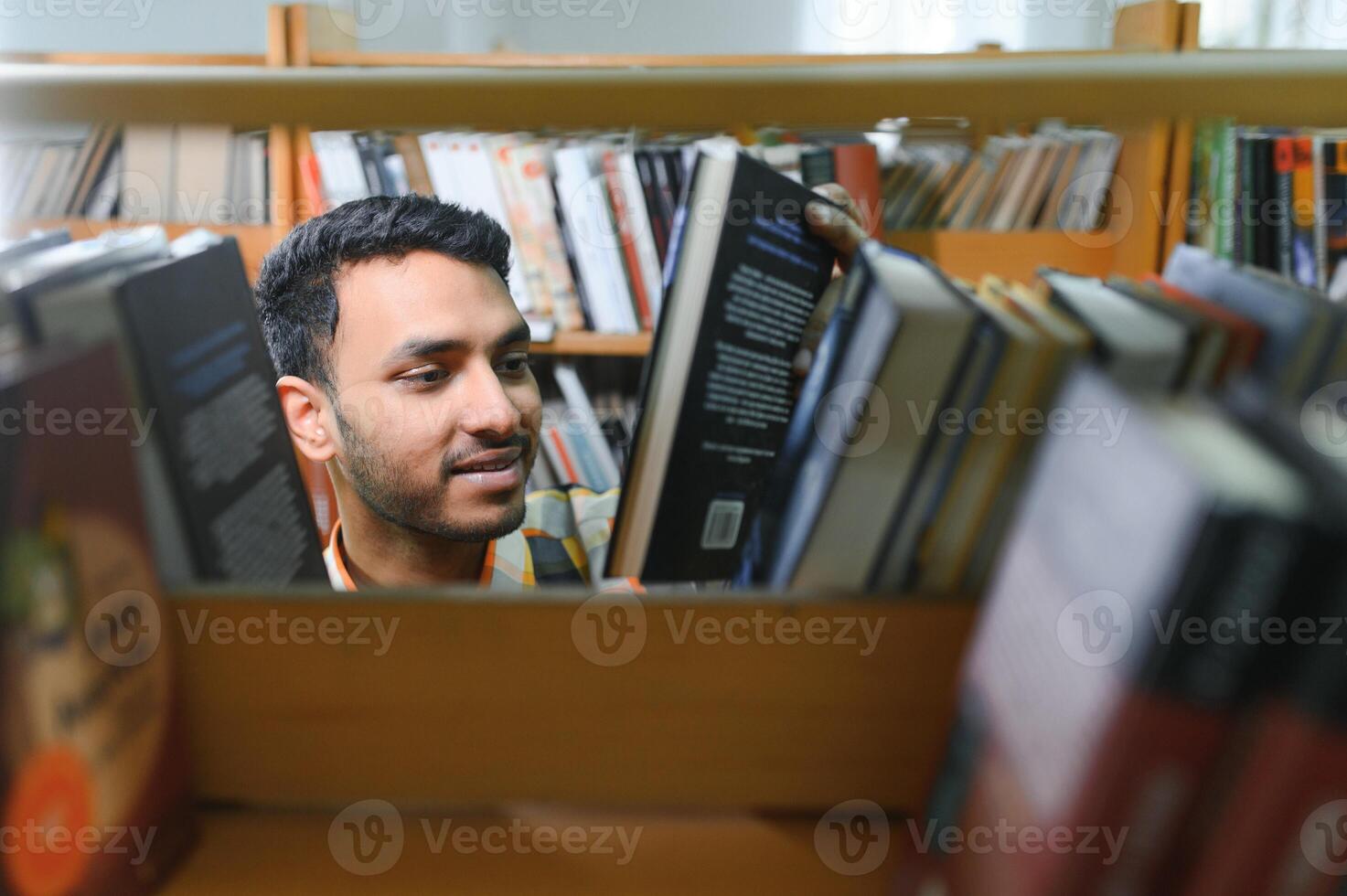 Masculin Indien étudiant à le bibliothèque avec livre photo