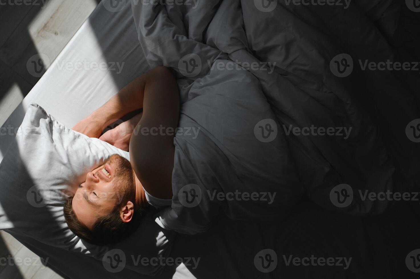 Beau homme en train de dormir en dessous de doux couverture dans lit à Accueil photo