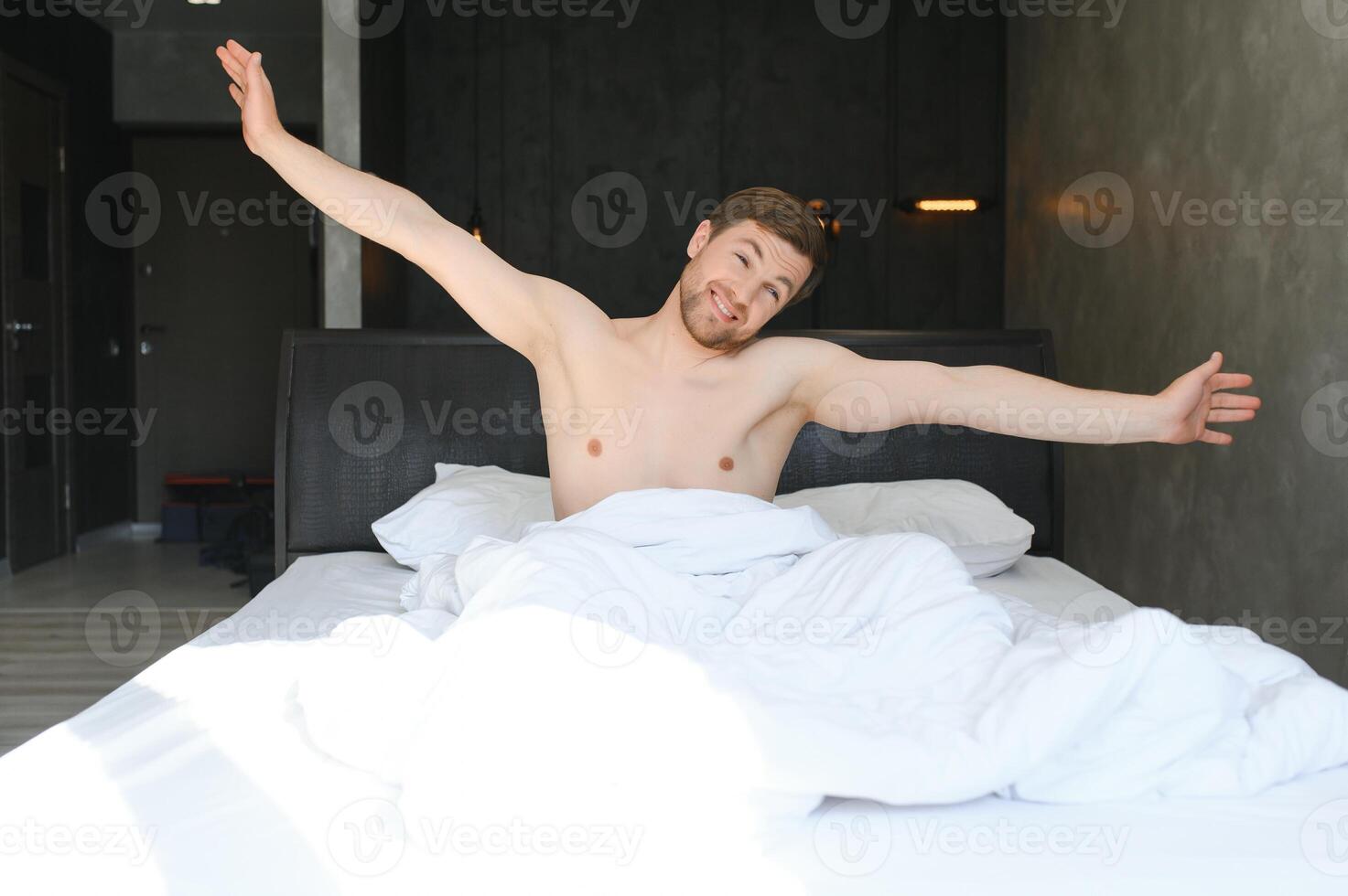 Jeune homme en train de dormir veille en haut et élongation dans le sien lit photo