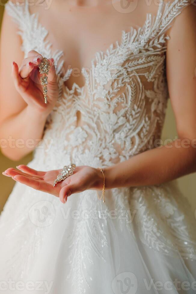 magnifique la mariée dans blanc mariage robe met sur boucle d'oreille. photo