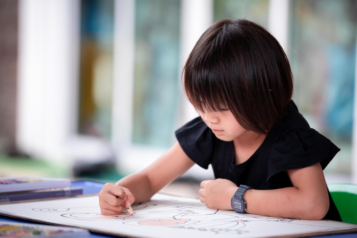 étudiante asiatique faisant de l'art sur grand papier. enfant tenant une couleur pastel à l'huile et une coloration amusante. enfant fait de l'artisanat à la maison. passe-temps avec activité à la maison. photo