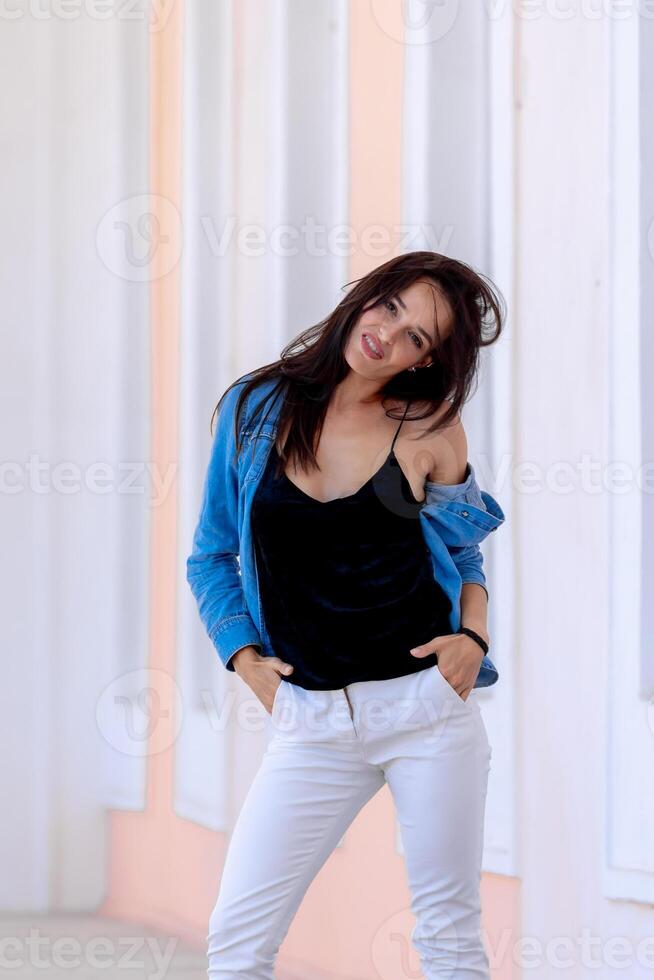 portrait de mignonne de bonne humeur souriant Jeune jolie femme dans décontractée jeans vêtements. permanent sur lumière salle Contexte. photo