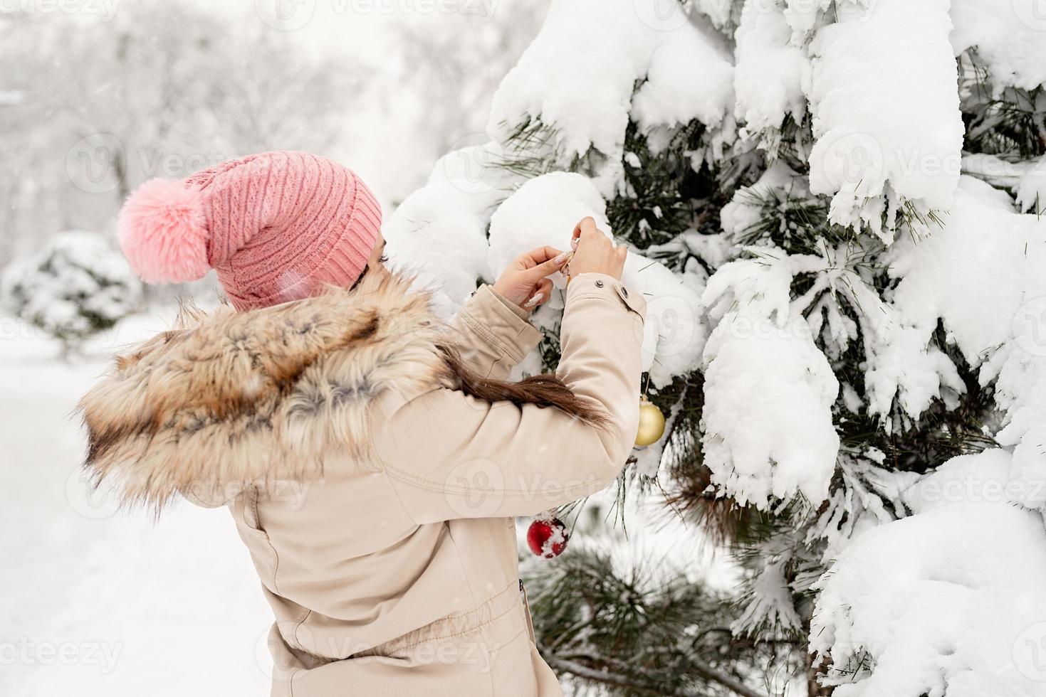 belle femme dans des vêtements d'hiver chauds décorant l'arbre de noël dans un parc en journée de neige photo