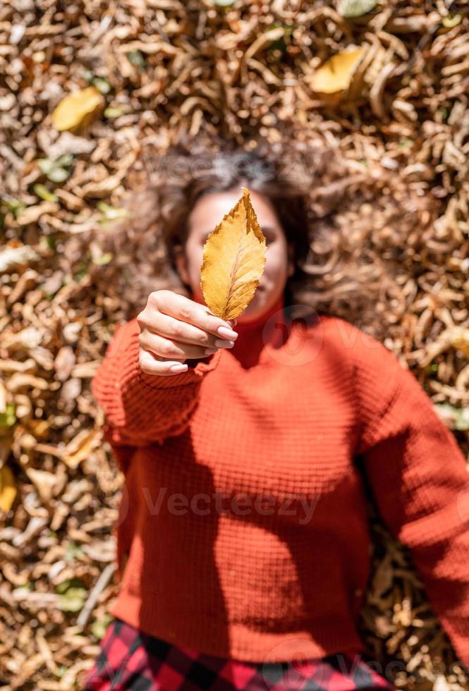 Jeune femme heureuse rassemblant des feuilles dans la forêt d'automne photo